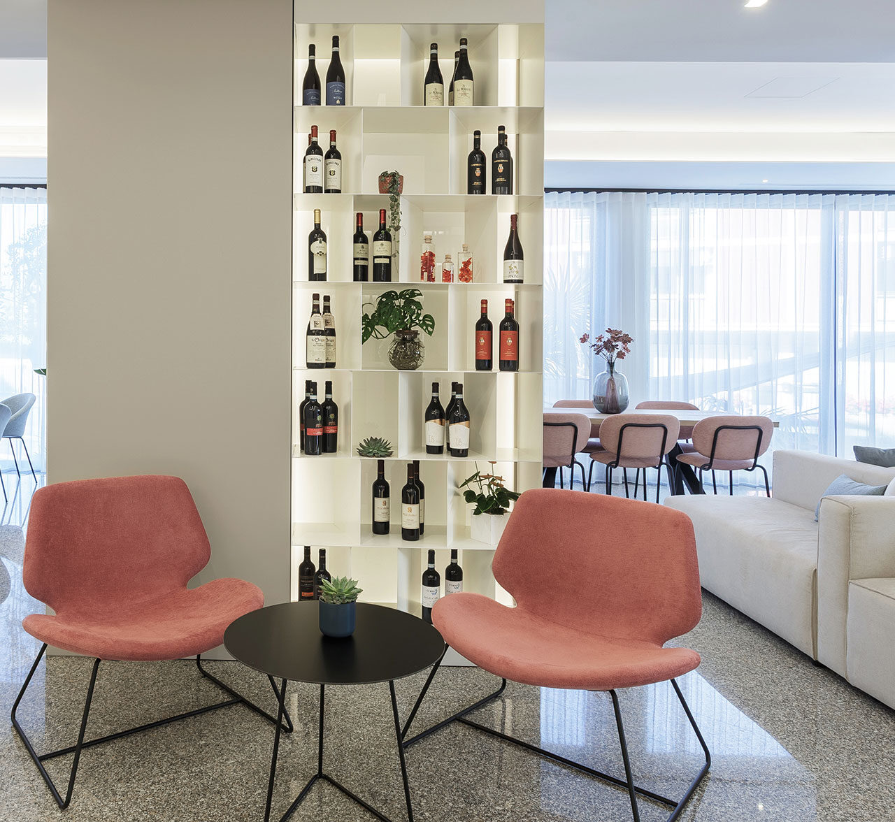 Arredamento su misura per lobby lounge hotel, scaffalatura divisoria su misura a giorno in finitura bianca, poltroncine colorate, divani bianchi, lampadari di design